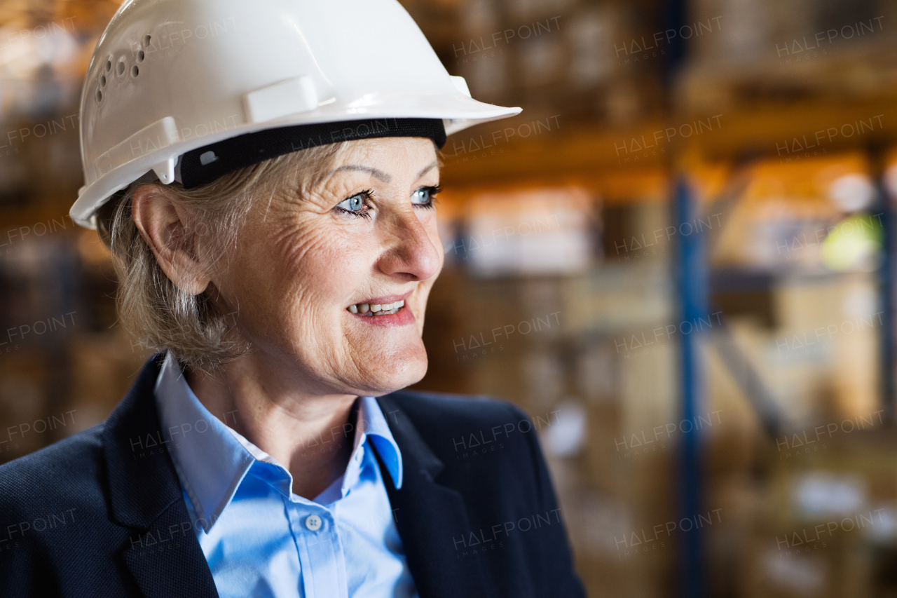 Portrait of a senior woman warehouse manager or supervisor with white helmet. Close up. Copy space.