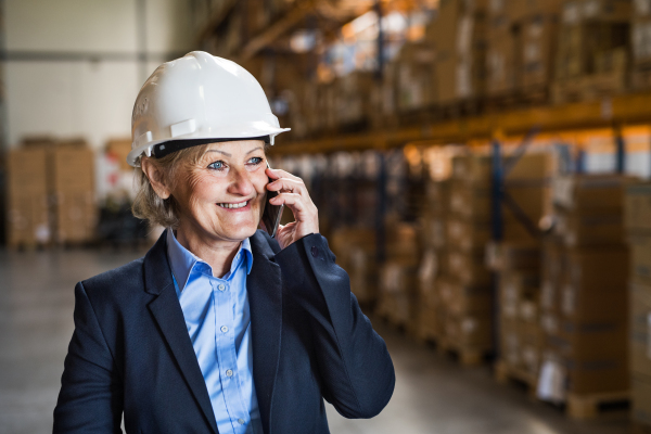 An attractive senior woman warehouse manager or supervisor with smartphone, making a phone call. Copy space.