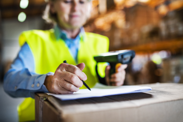 Unrecognizable warehouse woman worker or supervisor using a mobile handheld PC with barcode scanner.