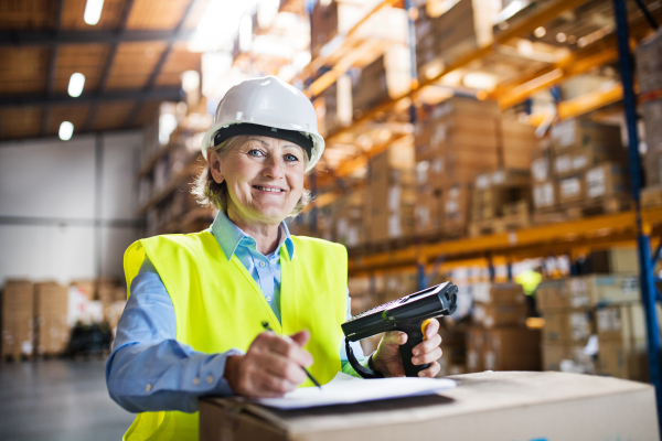 A senior warehouse woman worker or supervisor using a mobile handheld PC with barcode scanner.