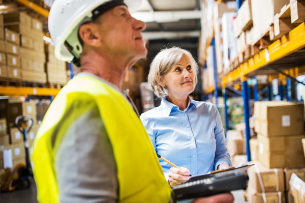 Senior woman manager and a man worker with barcode scanner working together in a warehouse.