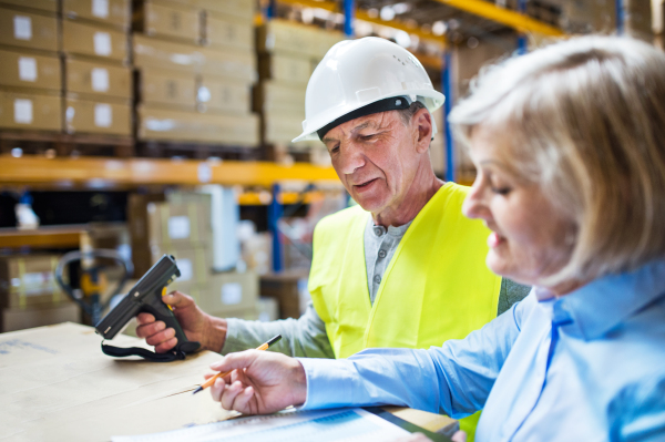 Senior woman manager and a man worker with barcode scanner working together in a warehouse.