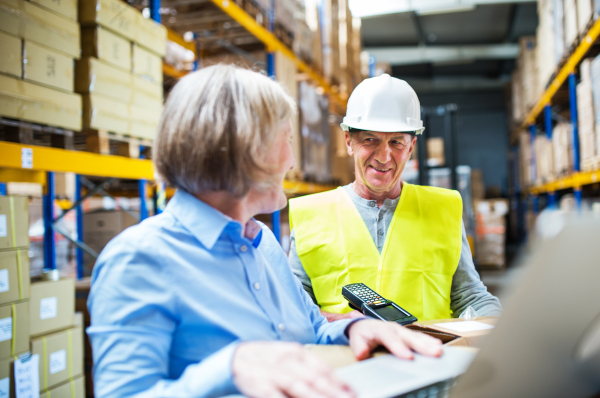 Senior woman manager and a man worker with barcode scanner working together in a warehouse.