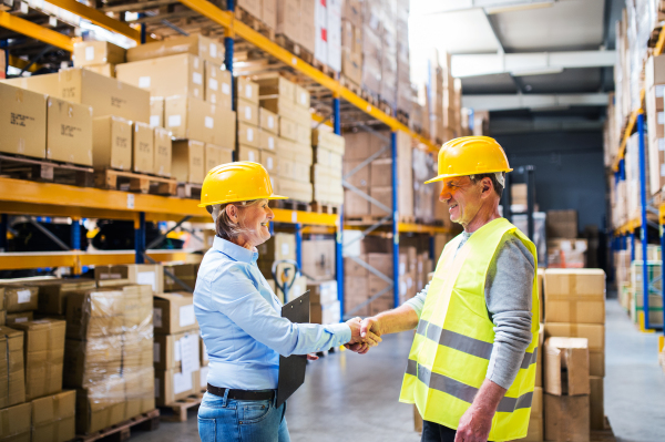 Senior woman manager and a man worker working together in a warehouse, shaking hands.