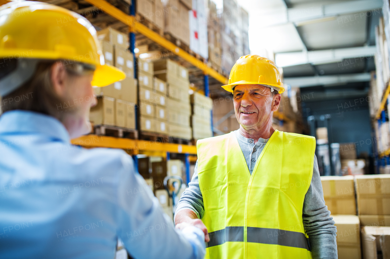 Senior woman manager and a man worker working together in a warehouse, shaking hands.