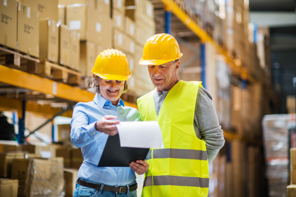 Senior woman manager with clipboard and a man worker working together in a warehouse.