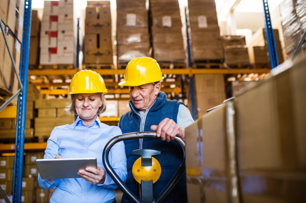 Senior woman manager and a man worker with a tablet working together in a warehouse.