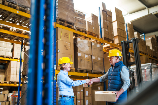 Senior woman manager and a man worker working together in a warehouse, shaking hands.