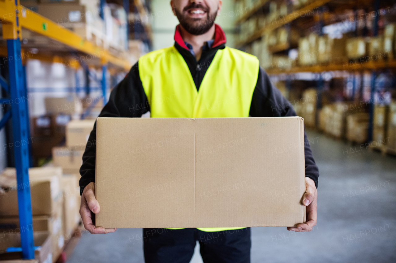 Unrecognizable young male warehouse worker holding a large box.