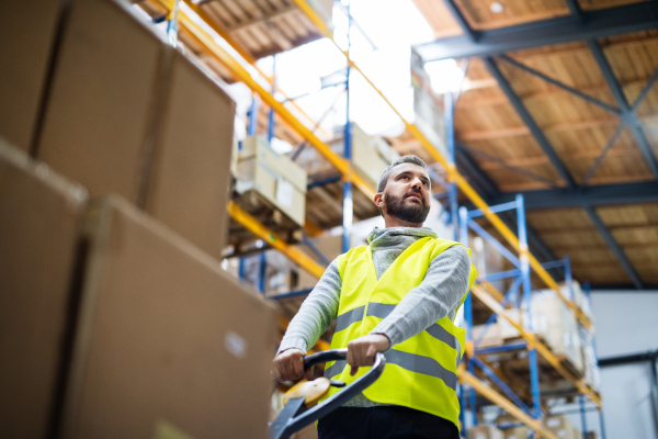 Young male warehouse worker pulling a pallet truck with boxes.