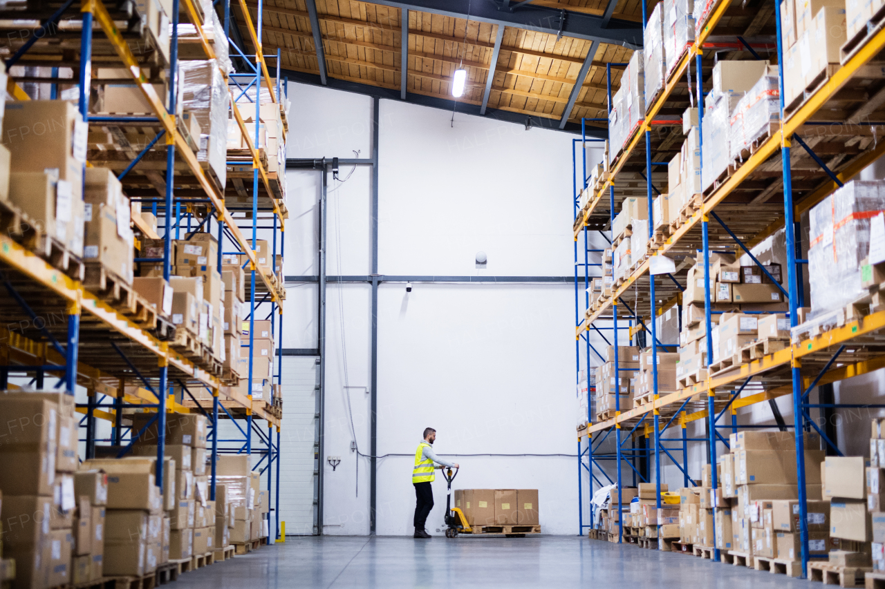 Young male warehouse worker pulling a pallet truck with boxes.