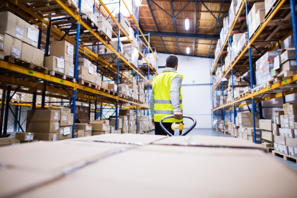 Young male warehouse worker pulling a pallet truck with boxes.