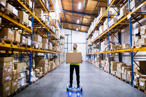 Male warehouse worker on hoverboard, holding a large box.