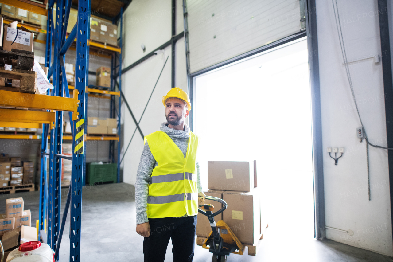 Young male warehouse worker pulling a pallet truck with boxes.