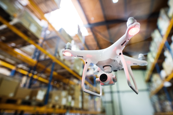 White drone flying inside the warehouse, under a wooden roof.