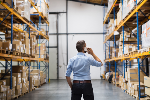 Warehouse worker or supervisor with a smartphone, making a phone call. Rear view.