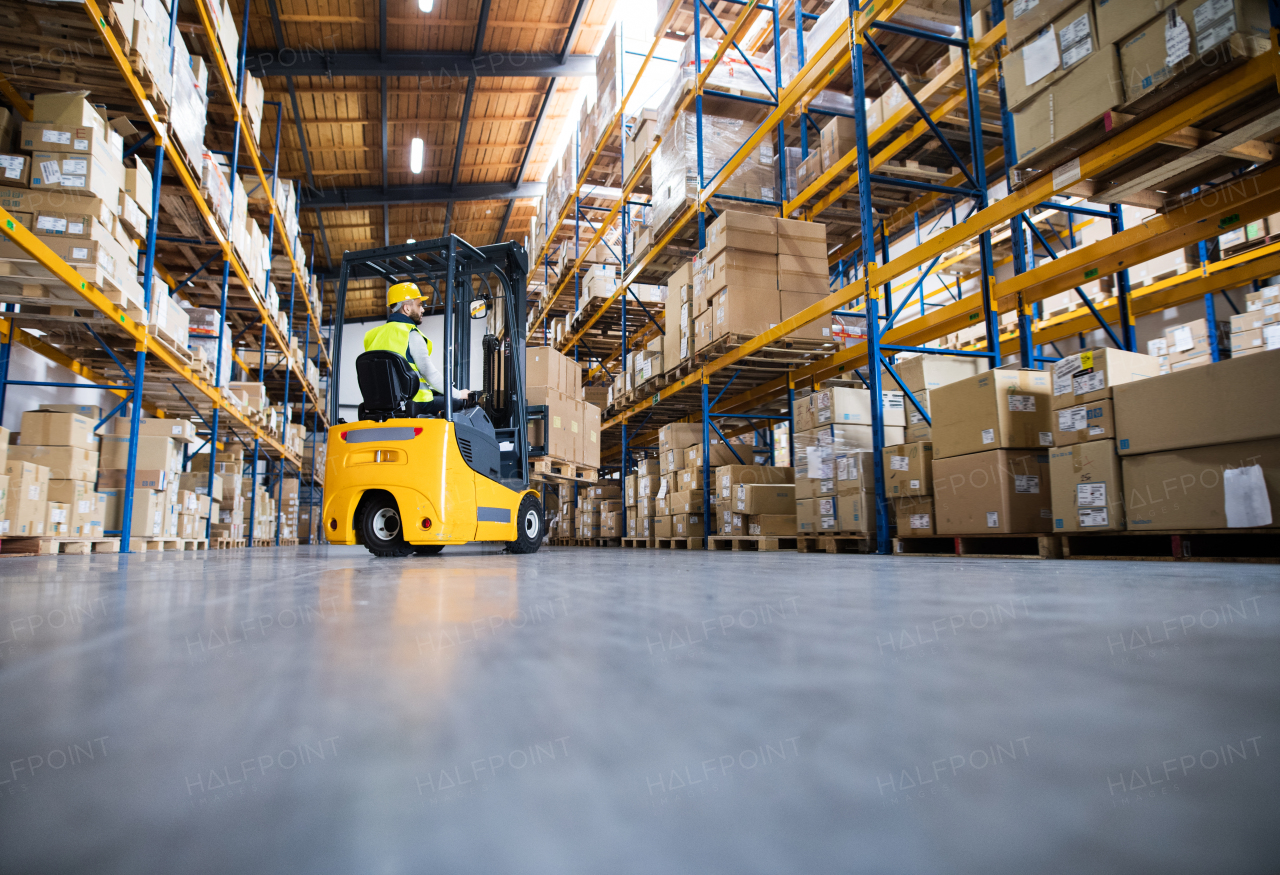 Young male worker lowering a pallet with boxes. Forklift driver working in a warehouse.