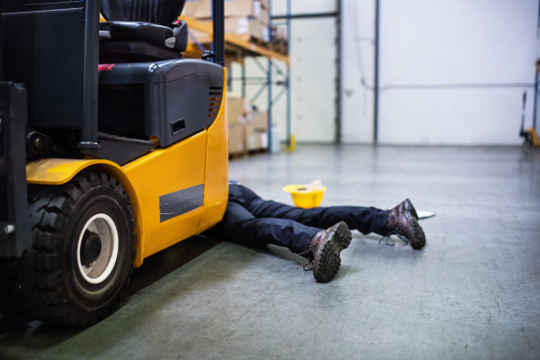 An accident in a warehouse. Unrecognizable man lying on the floor next to a forklift, unconscious.