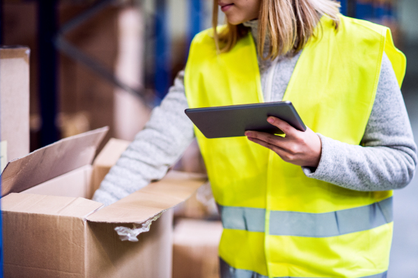 Unrecognizable young woman warehouse worker with tablet. A supervisor controlling stock.