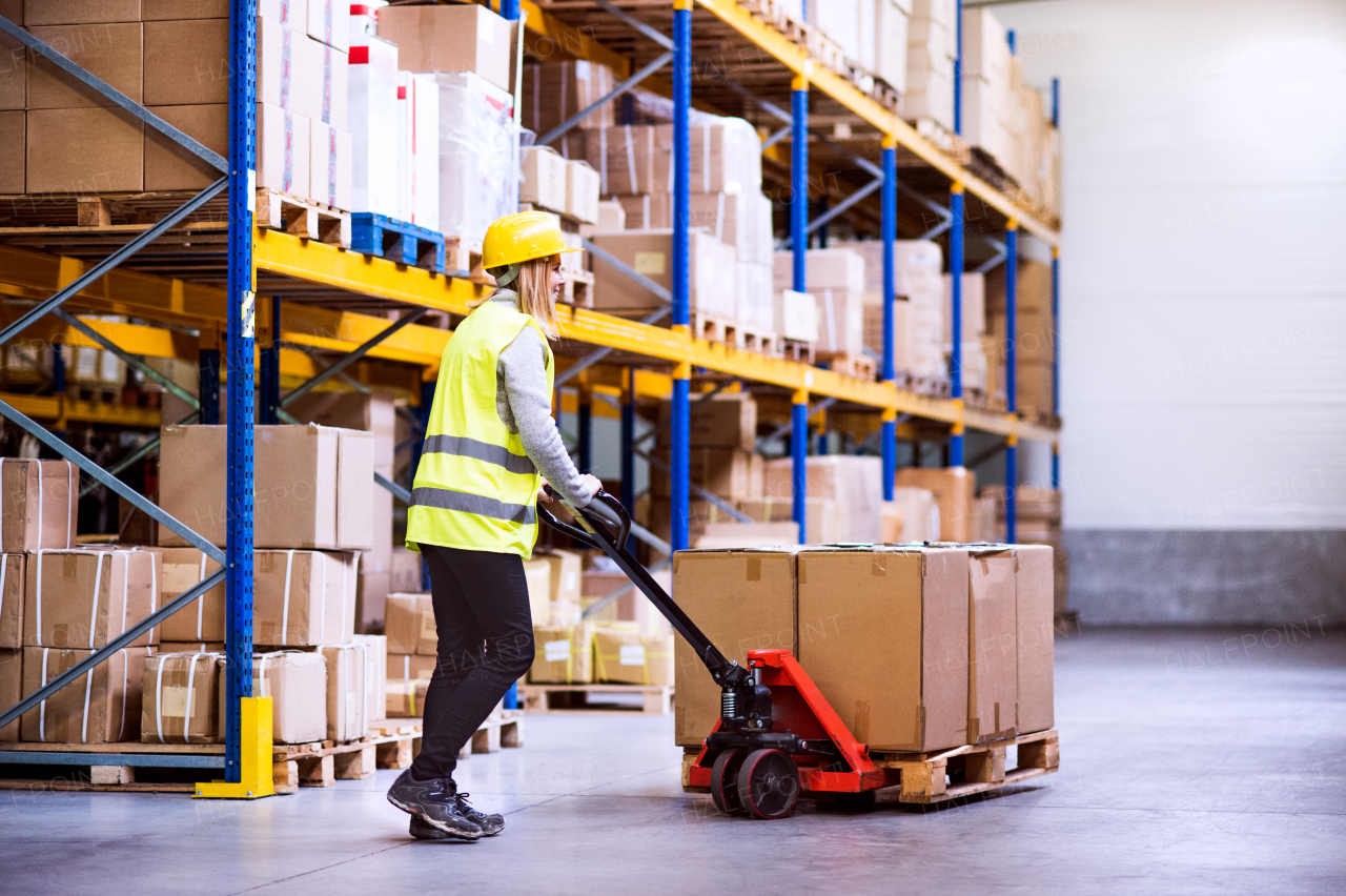 Young woman warehouse worker with hand forklift truck.