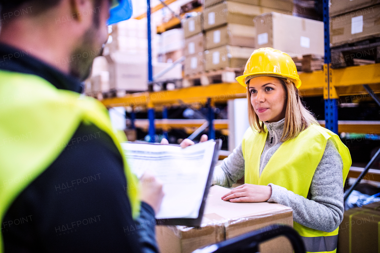 Young warehouse workers working together. Man and woman discussing something, making notes.