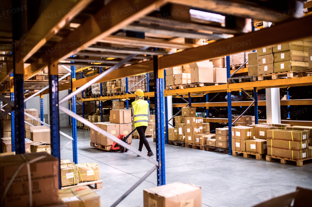 Young woman warehouse worker with hand forklift truck.