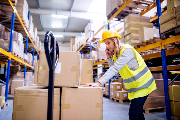 Young female warehouse worker with a smartphone. A woman or a supervisor making a phone call.