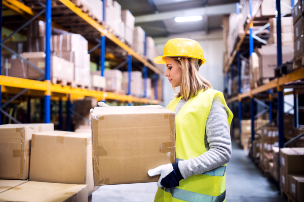 Young female warehouse worker loading up a pallet truck with boxes.