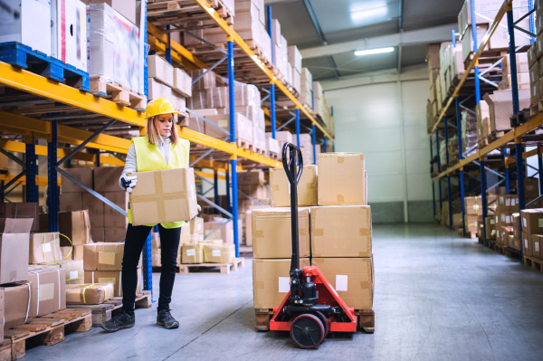 Young female warehouse worker loading up a pallet truck with boxes.