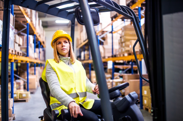 Beautiful young woman warehouse worker with forklift.