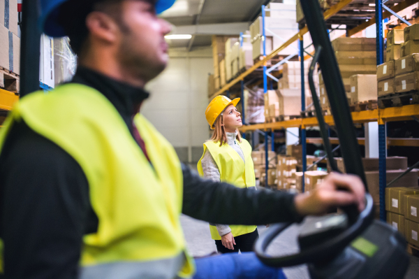 Young workers working together. Man forklift driver and a woman in a warehouse.