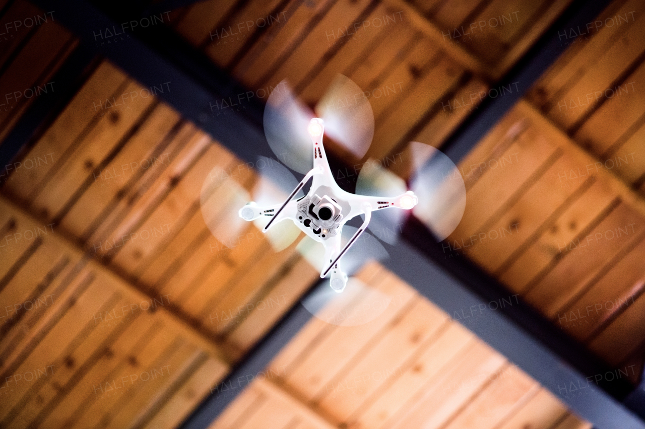 White drone flying inside the building, under a wooden roof.