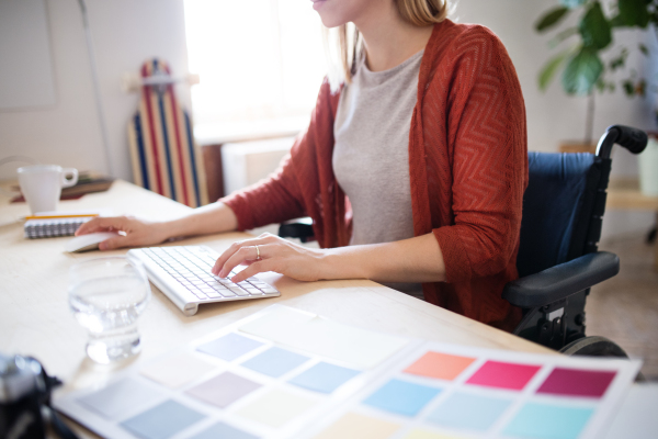 Unrecognizable businesswoman in wheelchair sitting at the desk, working.