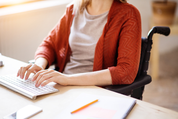 Unrecognizable businesswoman in wheelchair sitting at the desk, working.