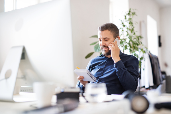 Businessman in wheelchair with smartphone at the desk in the office, making a phone call.