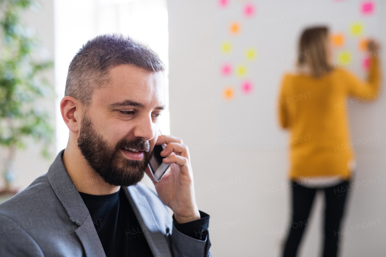 Two business people in the office working together. A man with smartphone, making a phone call.