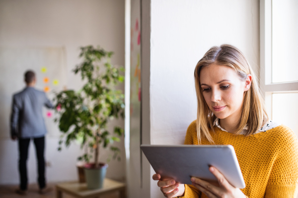 Two business people in the office working together. A woman with tablet reading.