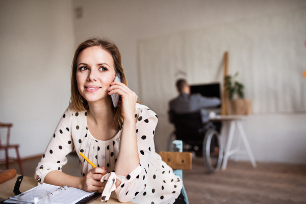 Two business people with wheelchair and smartphone working in the office.