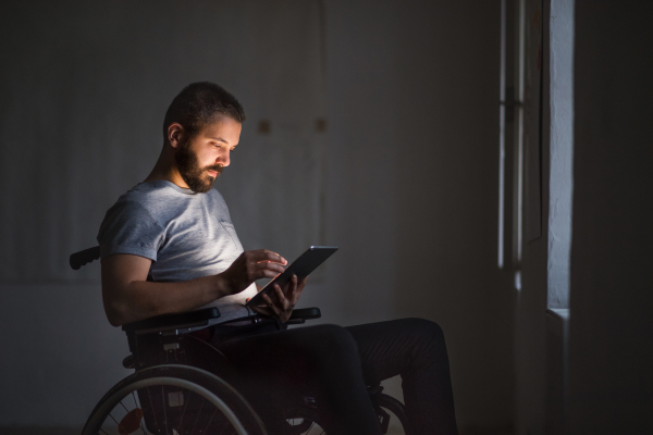 Handsome man in wheelchair working with tablet at home or in an office.