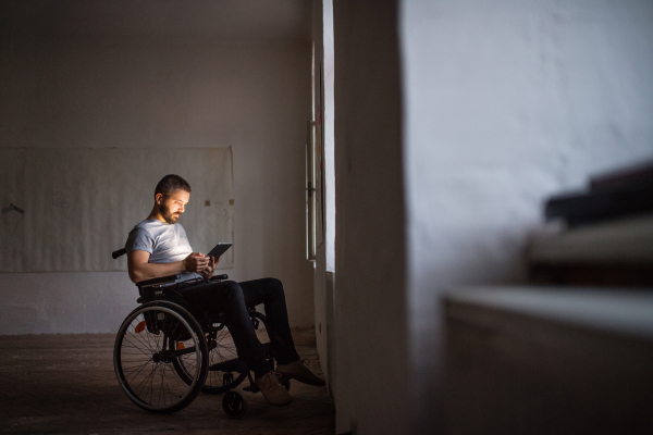 Man in wheelchair working with tablet at home or in an office.