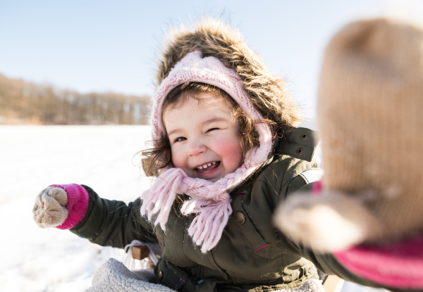 Cute little girl in green jacket and knitted hat an gloves playing outside in winter nature