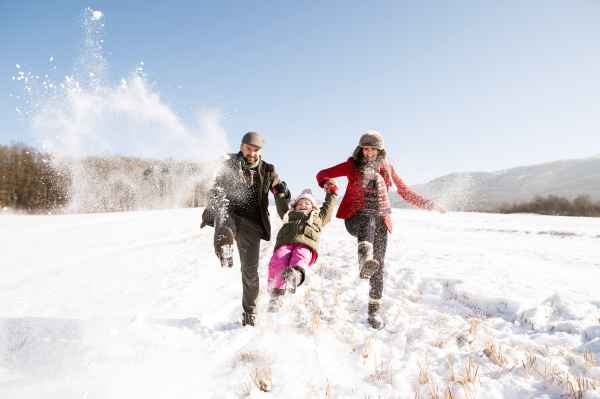 Father and mother having fun with their daughter, playing in the snow. Sunny white winter nature.