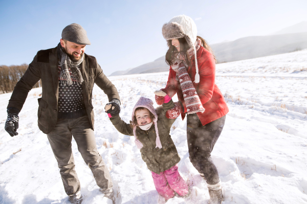 Father and mother having fun with their daughter, playing in the snow. Sunny white winter nature.