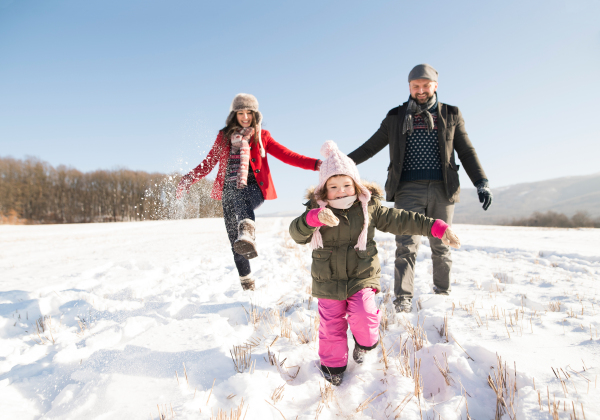 Father and mother having fun with their daughter, playing in the snow. Sunny white winter nature.