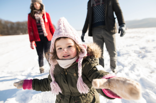 Unrecognizable father and mother having fun with their daughter, playing in the snow. Sunny white winter nature.