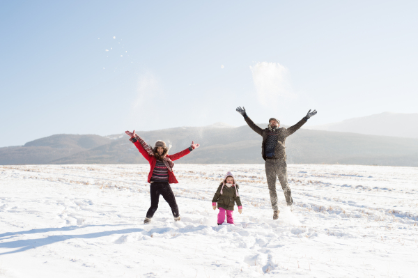 Father and mother having fun with their daughter, playing in the snow. Sunny white winter nature.