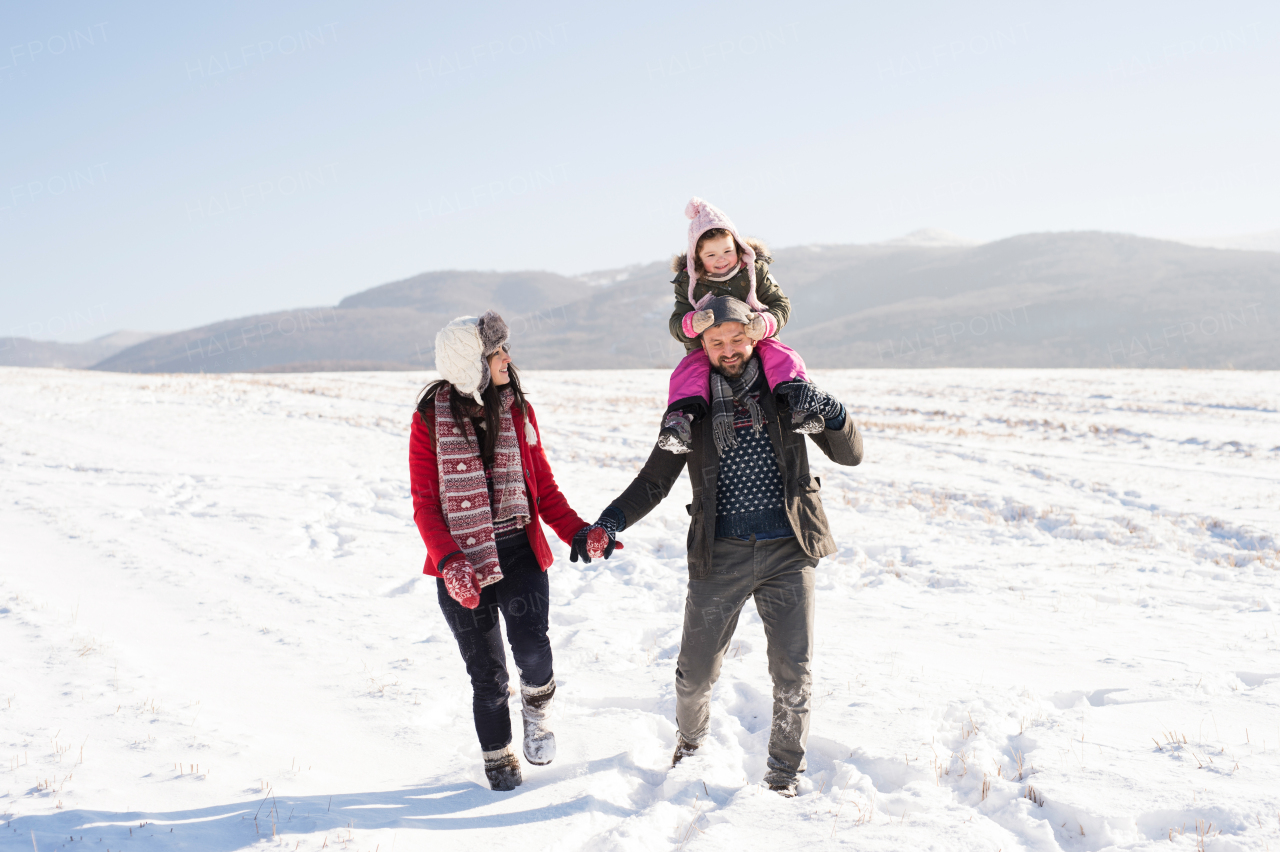 Father and mother having fun with their daughter, playing in the snow. Sunny white winter nature.