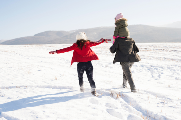 Father and mother having fun with their daughter, playing in the snow. Sunny white winter nature. Rear view.