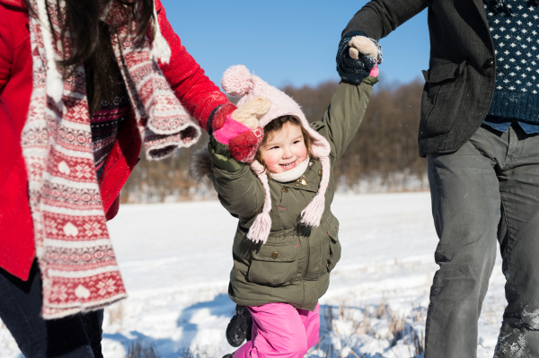 Unrecognizable father and mother having fun with their daughter, playing in the snow. Sunny white winter nature.