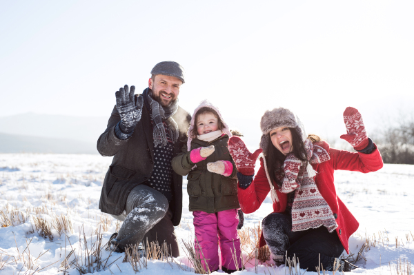 Father and mother having fun with their daughter, playing in the snow, waving. Sunny white winter nature.